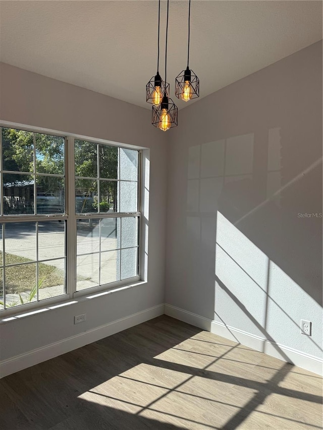 empty room featuring a healthy amount of sunlight, baseboards, and dark wood-type flooring