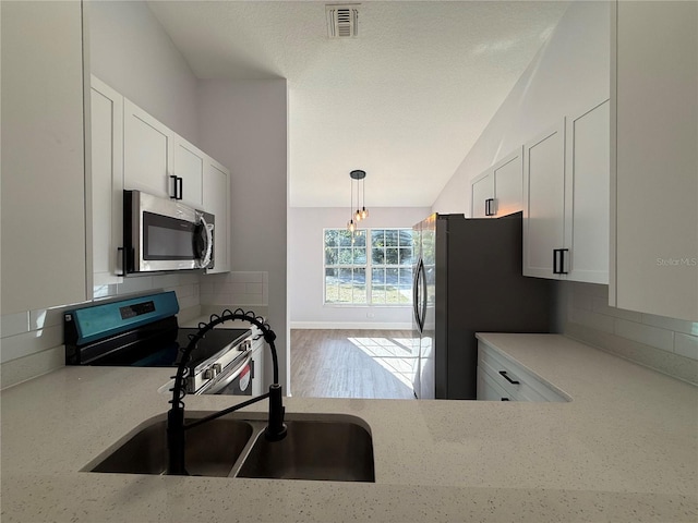 kitchen with stainless steel appliances, visible vents, white cabinetry, a sink, and light stone countertops