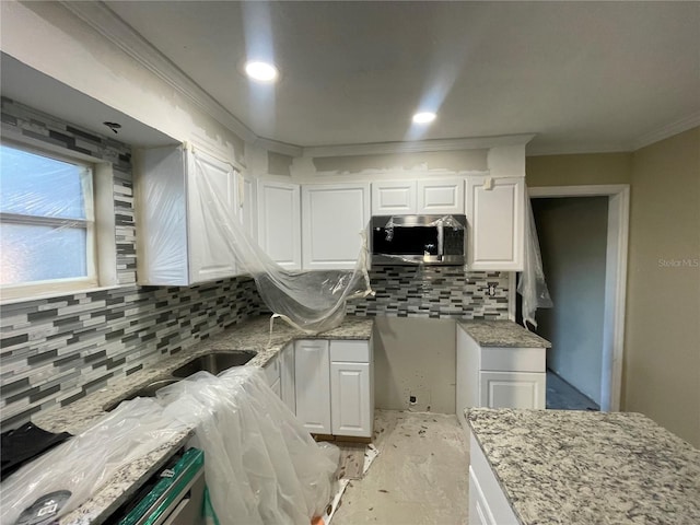 kitchen with white cabinets, backsplash, light stone counters, and ornamental molding