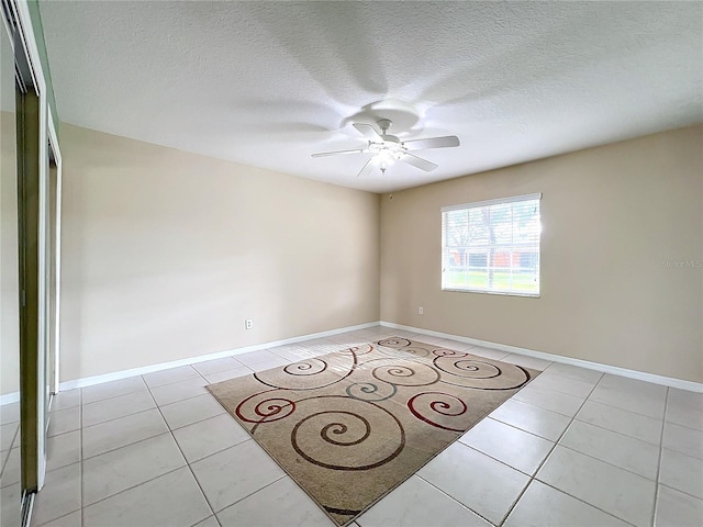 empty room with ceiling fan, light tile patterned floors, and a textured ceiling