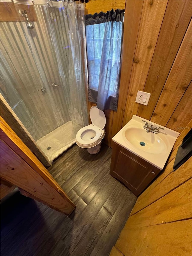 bathroom featuring vanity, a shower, wooden walls, hardwood / wood-style flooring, and toilet