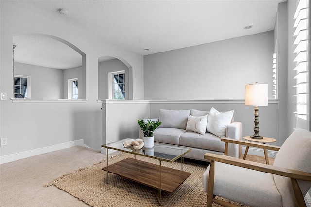 living area featuring arched walkways, carpet flooring, a textured ceiling, and baseboards