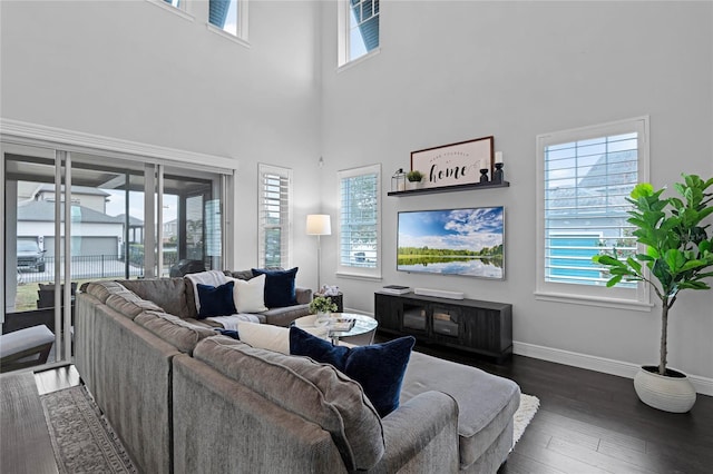 living area with a high ceiling, dark wood-style floors, and baseboards