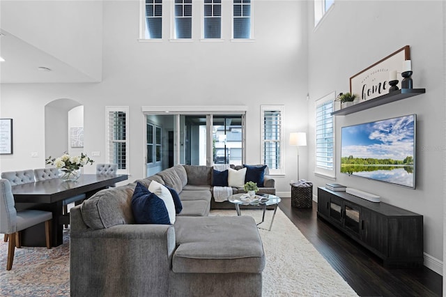 living area with dark wood finished floors, a high ceiling, baseboards, and arched walkways