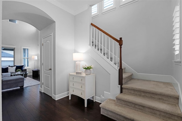 stairway featuring visible vents, arched walkways, a high ceiling, wood-type flooring, and baseboards