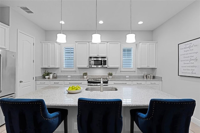 kitchen with a sink, a kitchen breakfast bar, appliances with stainless steel finishes, and a center island with sink