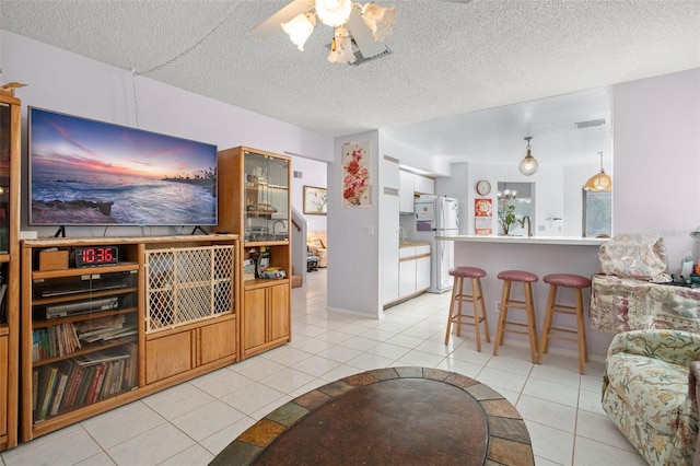 living room featuring ceiling fan, sink, light tile patterned floors, and a textured ceiling