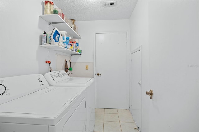 laundry area featuring light tile patterned floors, washer and dryer, and a textured ceiling