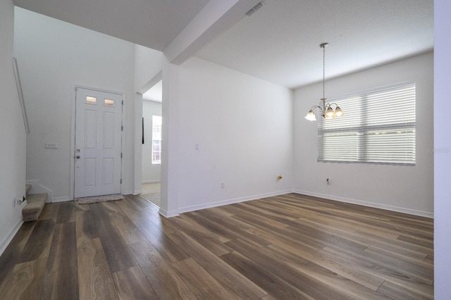 spare room with a chandelier, beamed ceiling, and dark wood-type flooring