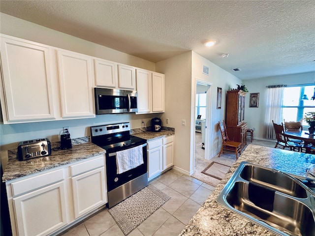 kitchen featuring visible vents, light tile patterned floors, appliances with stainless steel finishes, white cabinetry, and a sink