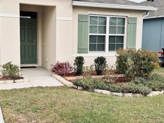 entrance to property with a lawn, roof with shingles, and stucco siding