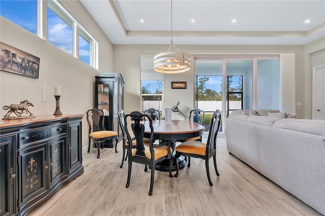 dining area featuring light wood-type flooring, a tray ceiling, an inviting chandelier, and a healthy amount of sunlight