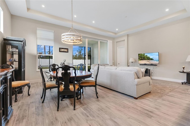 dining area featuring a tray ceiling, light hardwood / wood-style floors, and a notable chandelier