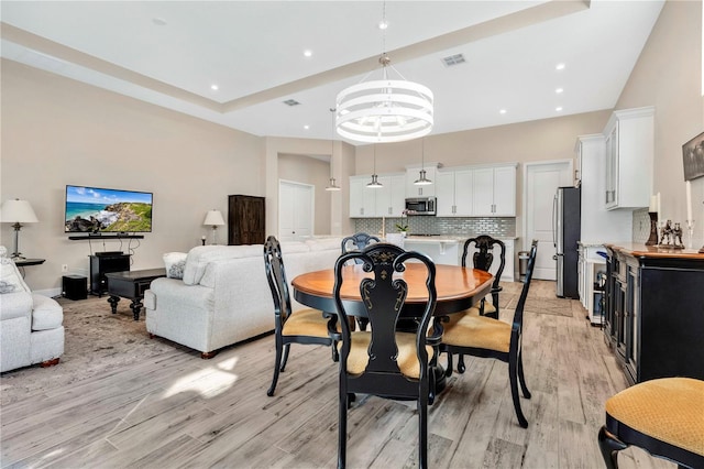 dining area featuring light wood-type flooring, a tray ceiling, and a chandelier