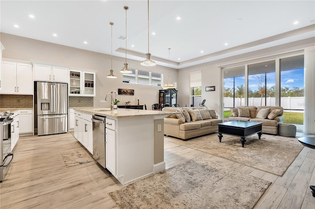 kitchen with appliances with stainless steel finishes, light stone counters, a kitchen island with sink, decorative light fixtures, and white cabinets