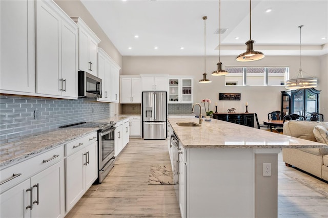 kitchen with white cabinetry, hanging light fixtures, stainless steel appliances, a raised ceiling, and a spacious island