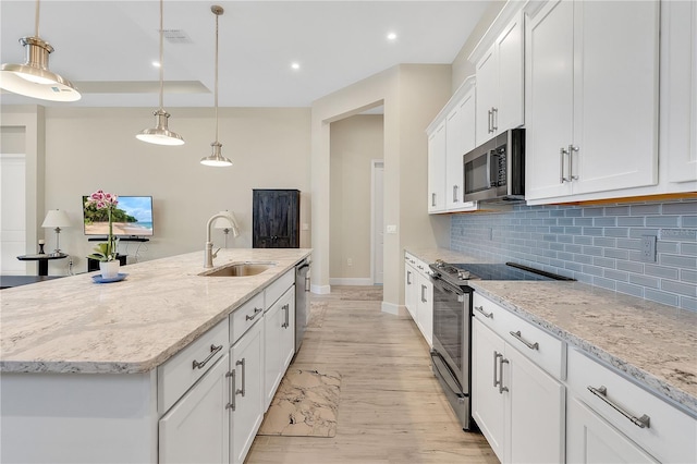 kitchen with pendant lighting, a kitchen island with sink, white cabinets, sink, and stainless steel appliances