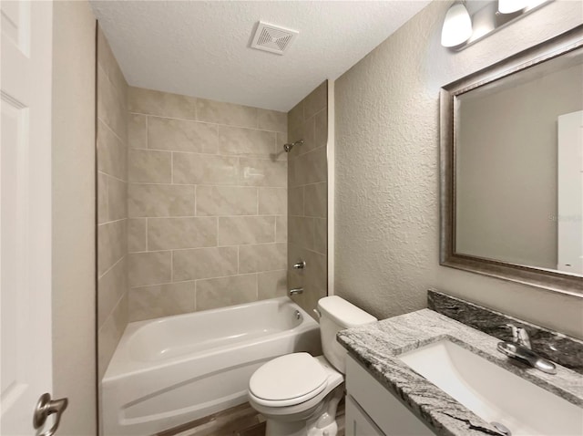 full bathroom featuring vanity, a textured ceiling, tiled shower / bath combo, hardwood / wood-style floors, and toilet