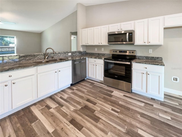 kitchen featuring appliances with stainless steel finishes, dark stone counters, vaulted ceiling, sink, and white cabinets