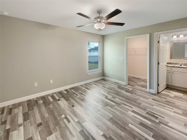 unfurnished bedroom with a walk in closet, ensuite bathroom, ceiling fan, light hardwood / wood-style flooring, and a closet