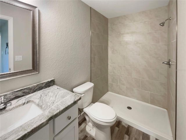 bathroom with tiled shower, vanity, wood-type flooring, and toilet