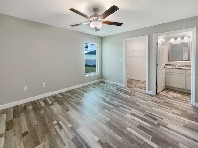 unfurnished bedroom featuring ensuite bath, ceiling fan, a spacious closet, light hardwood / wood-style floors, and a closet