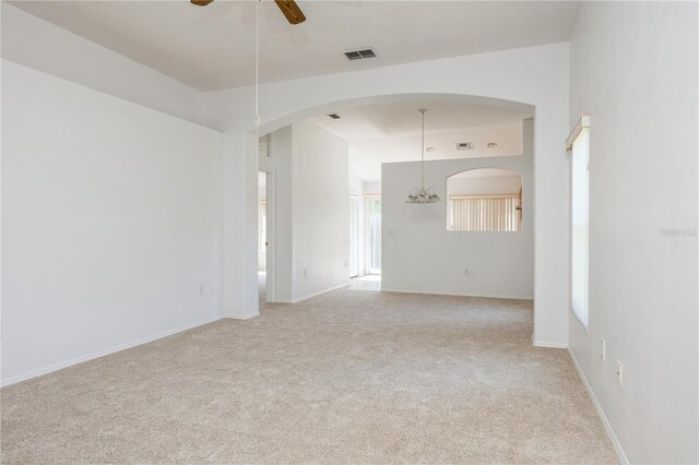 unfurnished room with visible vents, baseboards, light colored carpet, and ceiling fan with notable chandelier