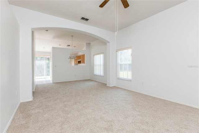 empty room featuring visible vents, light carpet, baseboards, and ceiling fan