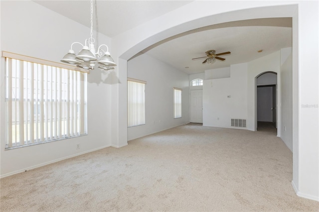 carpeted empty room with baseboards, ceiling fan with notable chandelier, visible vents, and arched walkways