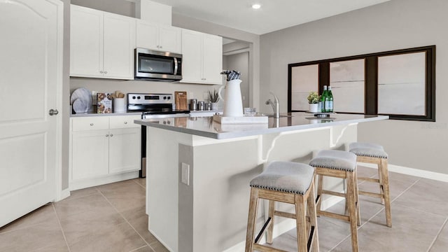 kitchen with white cabinets, a kitchen bar, an island with sink, and appliances with stainless steel finishes