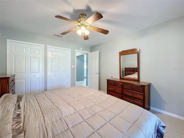 bedroom featuring light carpet, a textured ceiling, ceiling fan, and multiple closets