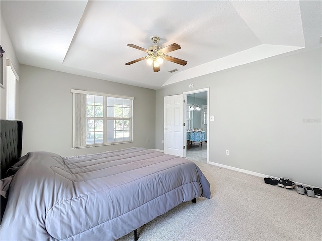 bedroom featuring a tray ceiling, ceiling fan, ensuite bathroom, and light carpet