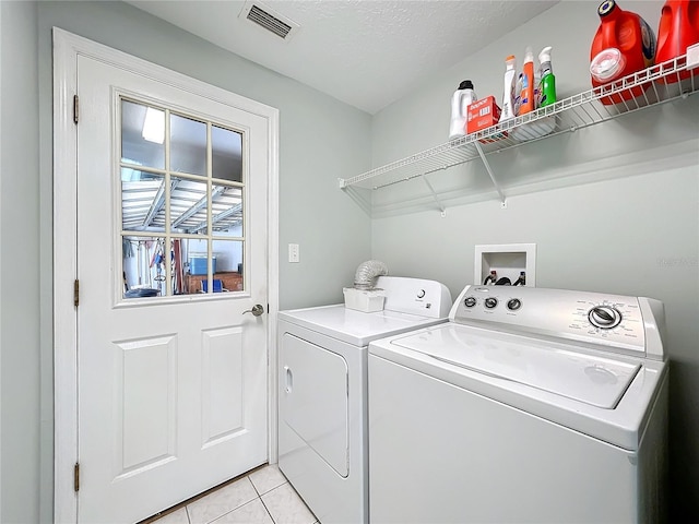 clothes washing area featuring light tile patterned floors, washer and dryer, and a textured ceiling