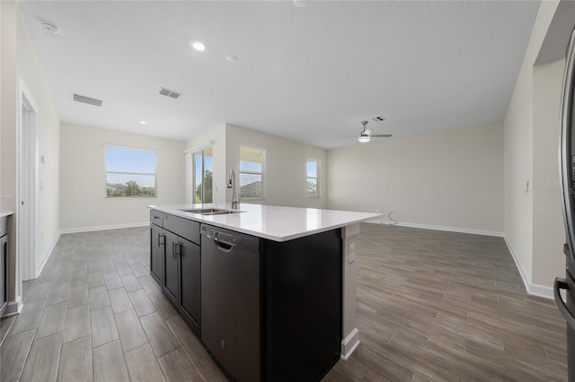 kitchen featuring stainless steel dishwasher, a textured ceiling, ceiling fan, sink, and a center island with sink