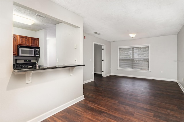 kitchen with dark hardwood / wood-style floors, a textured ceiling, kitchen peninsula, a breakfast bar area, and stainless steel appliances