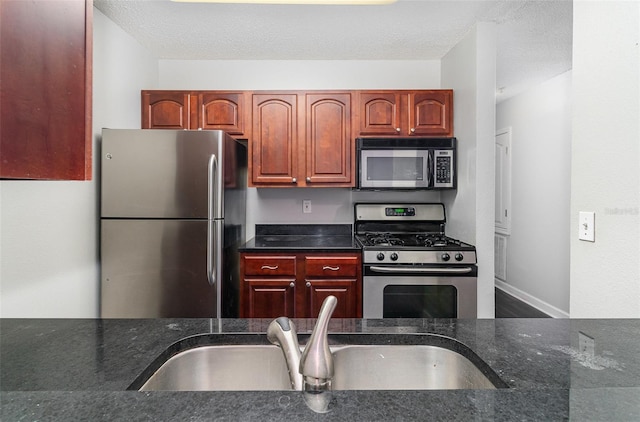 kitchen with dark stone counters, sink, stainless steel appliances, and a textured ceiling