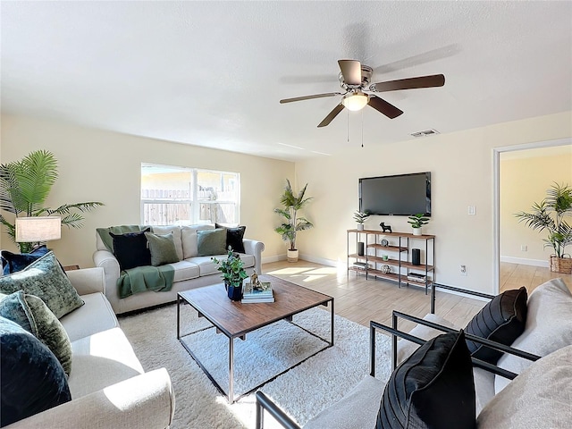 living room featuring light wood-type flooring, baseboards, visible vents, and a ceiling fan