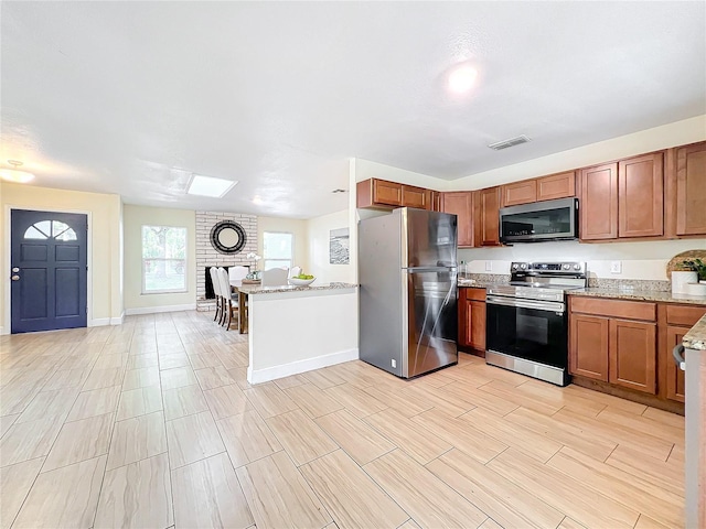 kitchen featuring light stone countertops, visible vents, appliances with stainless steel finishes, and brown cabinetry