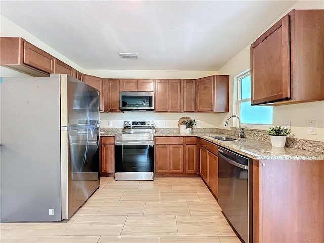 kitchen featuring visible vents, appliances with stainless steel finishes, brown cabinets, light stone counters, and a sink