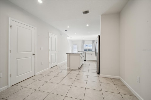 kitchen featuring stainless steel fridge, a center island, light tile patterned floors, and white cabinets