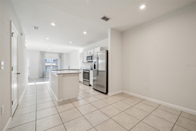 kitchen with white cabinetry, stainless steel appliances, light tile patterned flooring, and a kitchen island