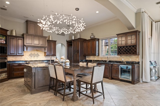 kitchen featuring backsplash, pendant lighting, a center island with sink, dark stone countertops, and wine cooler