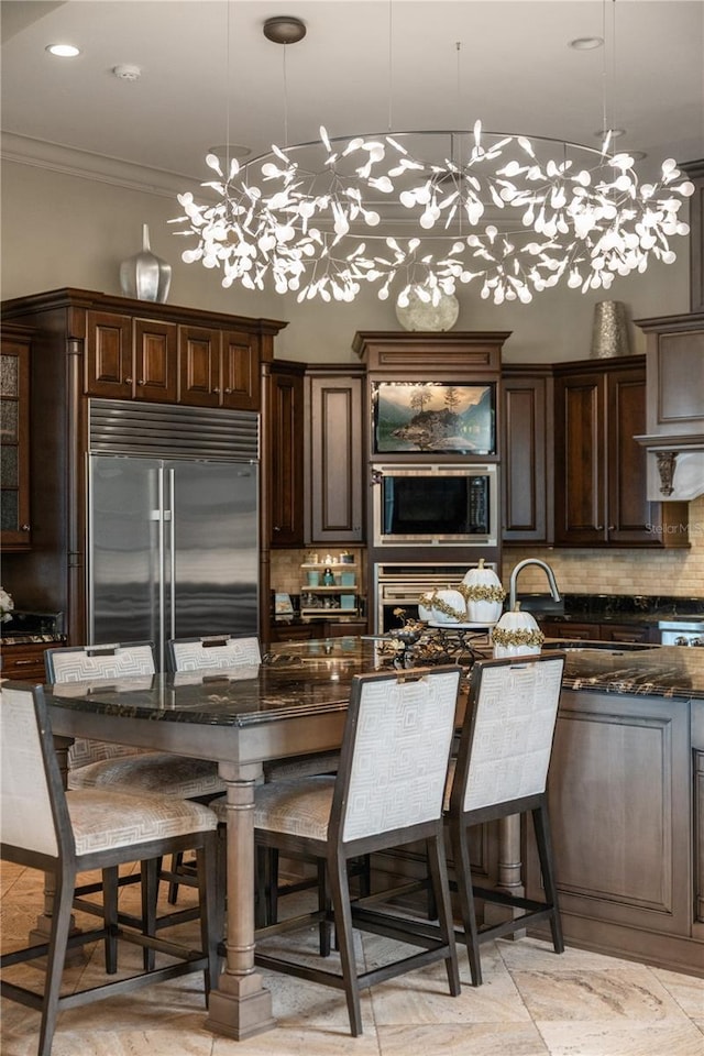 kitchen with built in appliances, decorative light fixtures, and dark stone countertops