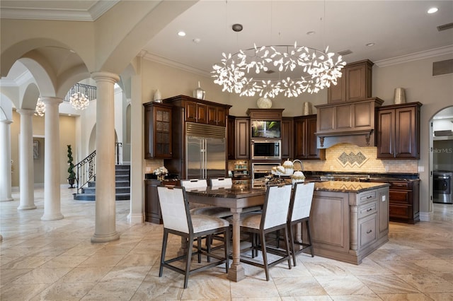 kitchen featuring dark stone counters, hanging light fixtures, built in appliances, a kitchen island, and dark brown cabinetry