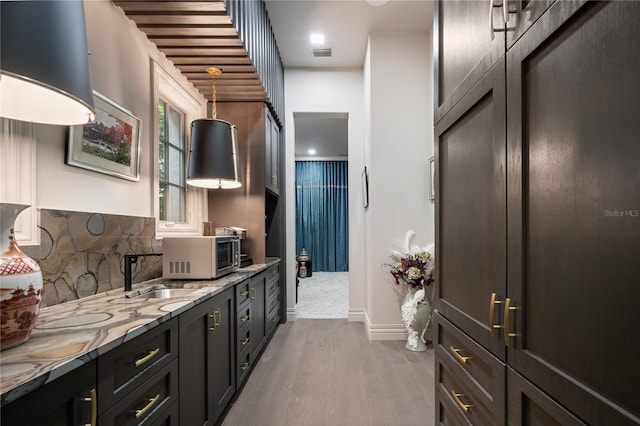 kitchen featuring pendant lighting, sink, dark hardwood / wood-style floors, decorative backsplash, and light stone counters