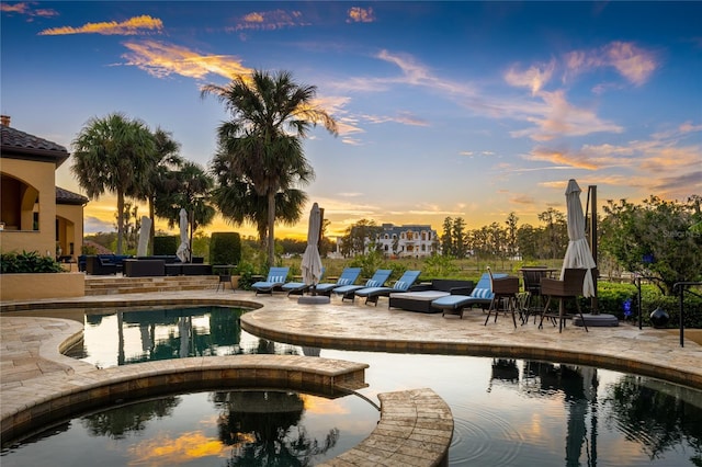 pool at dusk with an in ground hot tub and a patio