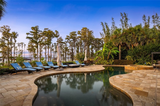 pool at dusk with an in ground hot tub and a patio