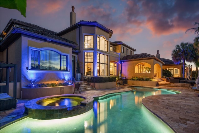 back house at dusk with a swimming pool with hot tub and a patio area