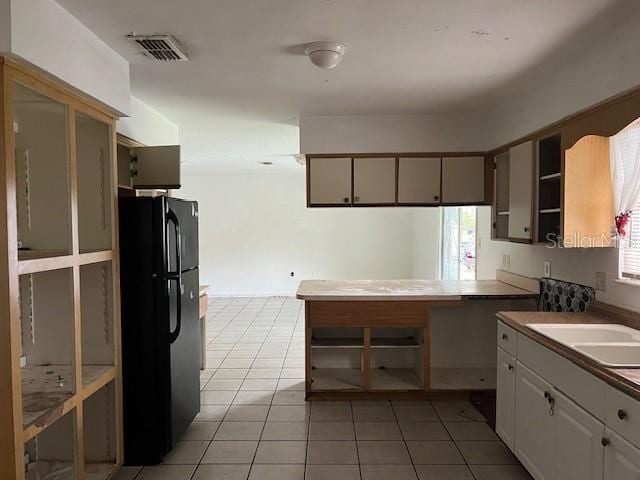 kitchen with sink, white cabinets, black fridge, kitchen peninsula, and light tile patterned floors