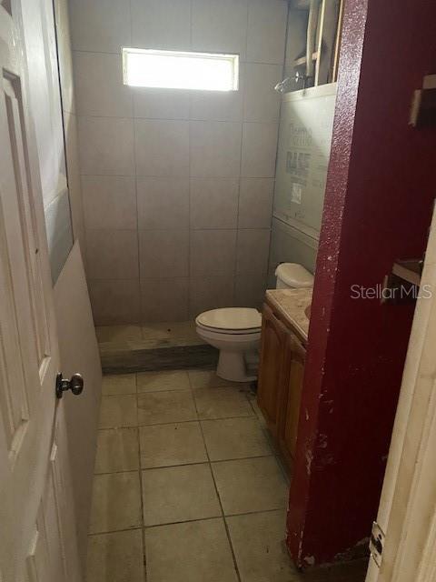 bathroom with tile patterned flooring, vanity, toilet, and tiled shower